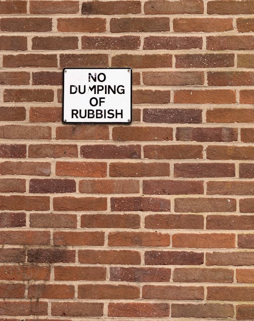 A rectangular white metal sign with black lettering mounted on a red brick wall. The sign reads