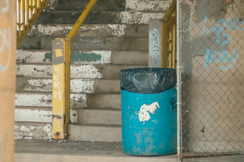 A weathered concrete staircase with uneven, stained steps leads upward, flanked on the left by a yellow metal handrail showing chipped paint and rust patches. Adjacent to the base of the stairs, a lar